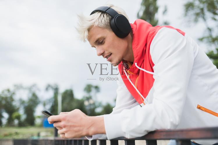 帅气的白人男子在智能手机上通过社交网络发信息戴着耳机听音乐和在
